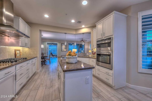 kitchen with stainless steel appliances, wall chimney range hood, wood finish floors, and visible vents