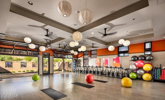workout area with a ceiling fan, a raised ceiling, and wood finished floors