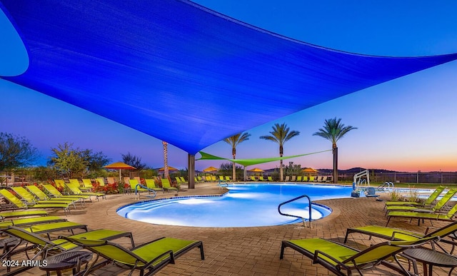 pool at dusk with a patio, a community pool, and fence