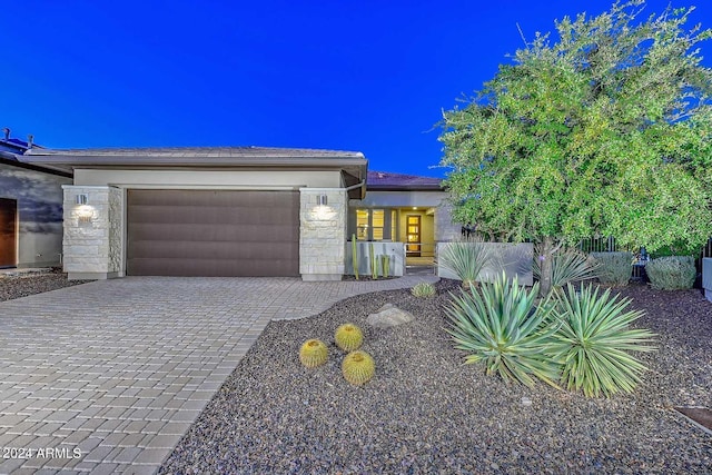 view of front of property with an attached garage, stone siding, fence, and decorative driveway