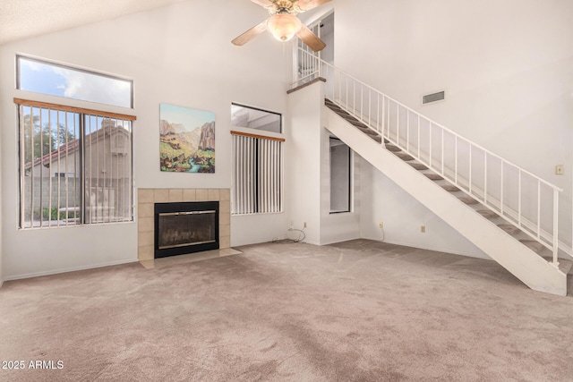 unfurnished living room featuring a tiled fireplace, a towering ceiling, carpet floors, and ceiling fan