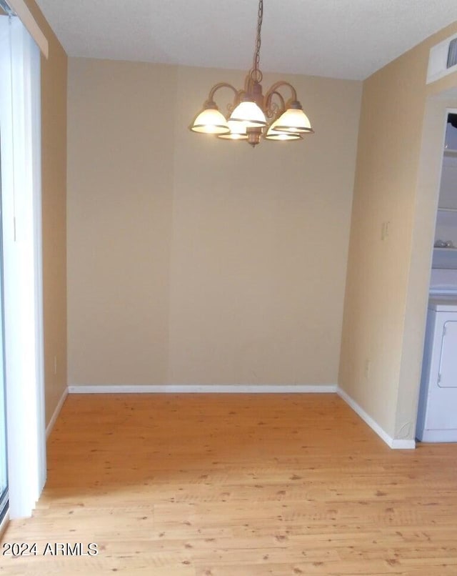 unfurnished dining area with washer / clothes dryer, an inviting chandelier, and light wood-type flooring