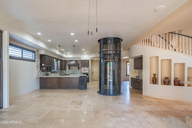 kitchen with tasteful backsplash, pendant lighting, dark brown cabinets, and custom exhaust hood