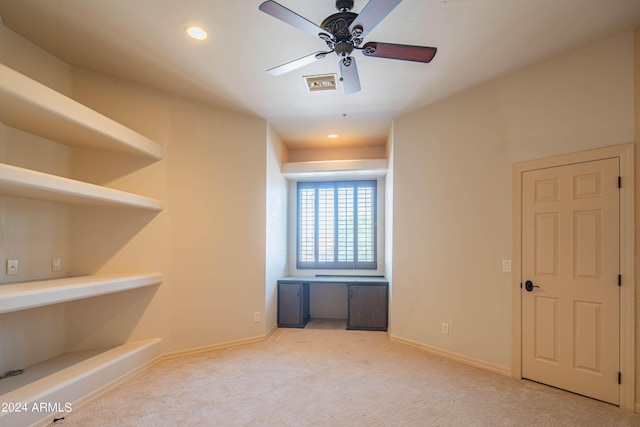 carpeted empty room with built in desk and ceiling fan