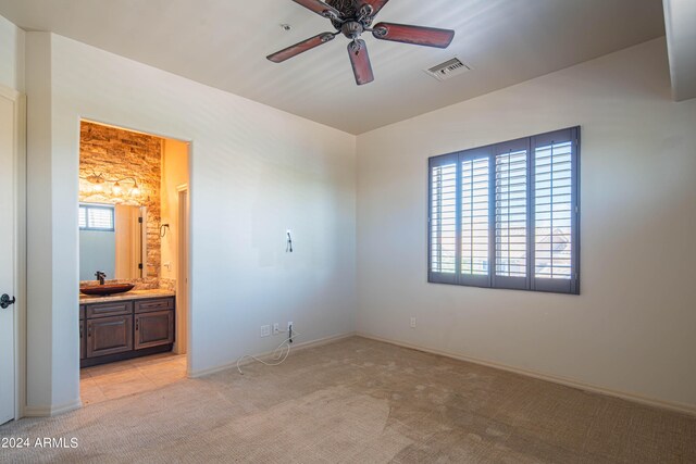 unfurnished bedroom featuring ceiling fan, sink, light colored carpet, and ensuite bath