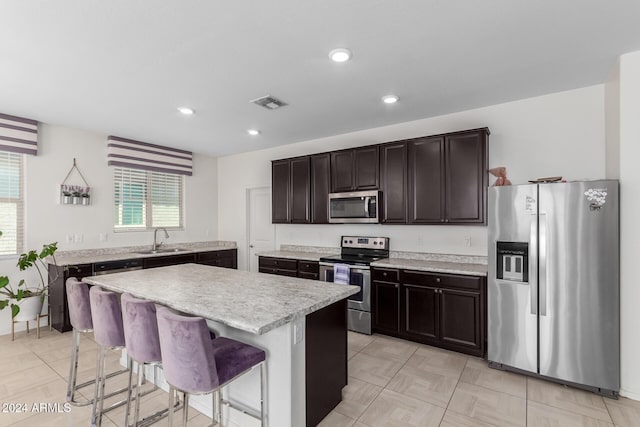 kitchen with sink, dark brown cabinets, a kitchen island, a kitchen bar, and stainless steel appliances