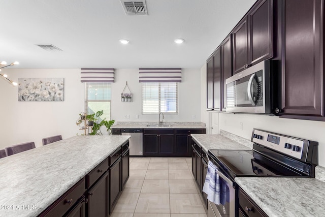 kitchen featuring dark brown cabinetry, sink, stainless steel appliances, a kitchen breakfast bar, and light tile patterned flooring