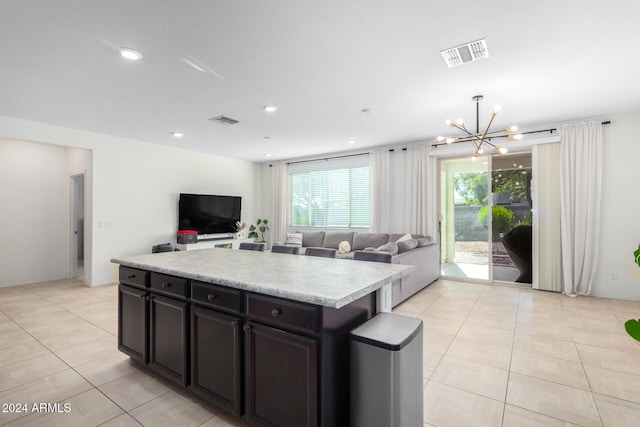 kitchen with dark brown cabinetry, a center island, light tile patterned floors, and an inviting chandelier