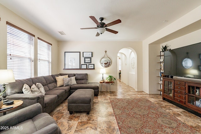 living area featuring stone finish flooring, arched walkways, visible vents, and ceiling fan