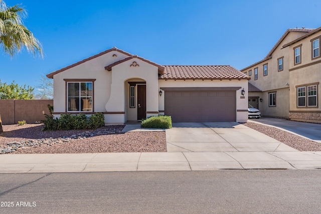 mediterranean / spanish home featuring stucco siding, a tile roof, fence, concrete driveway, and a garage