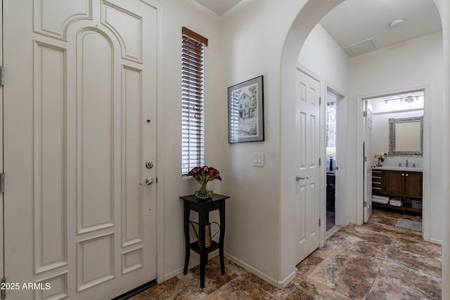 foyer featuring baseboards, arched walkways, and stone finish flooring