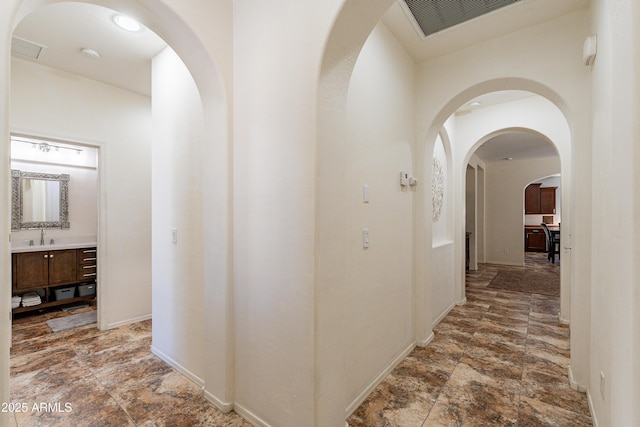 corridor with visible vents, stone finish floor, baseboards, and a sink