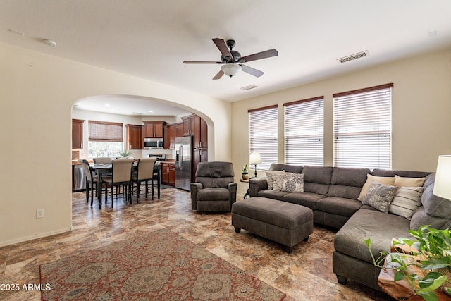 living area featuring baseboards, arched walkways, visible vents, and ceiling fan