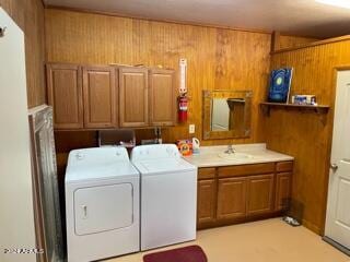 laundry area with wood walls, washer and clothes dryer, and cabinets