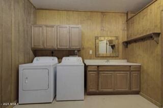 clothes washing area featuring cabinets, independent washer and dryer, wooden walls, and sink