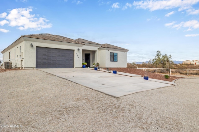 view of front of property with fence, concrete driveway, stucco siding, central AC unit, and an attached garage