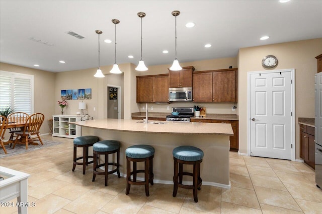 kitchen with sink, appliances with stainless steel finishes, a kitchen breakfast bar, decorative light fixtures, and a kitchen island with sink