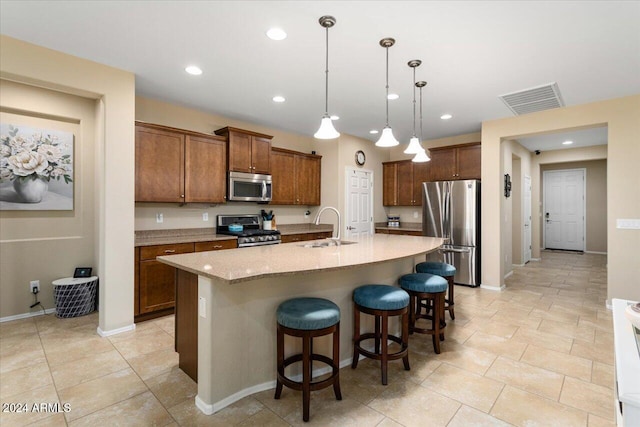 kitchen with sink, a breakfast bar, appliances with stainless steel finishes, an island with sink, and hanging light fixtures