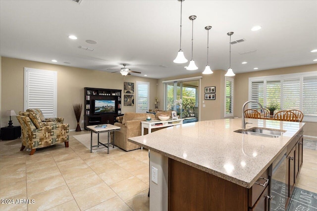 kitchen with a center island with sink, sink, decorative light fixtures, and light stone countertops