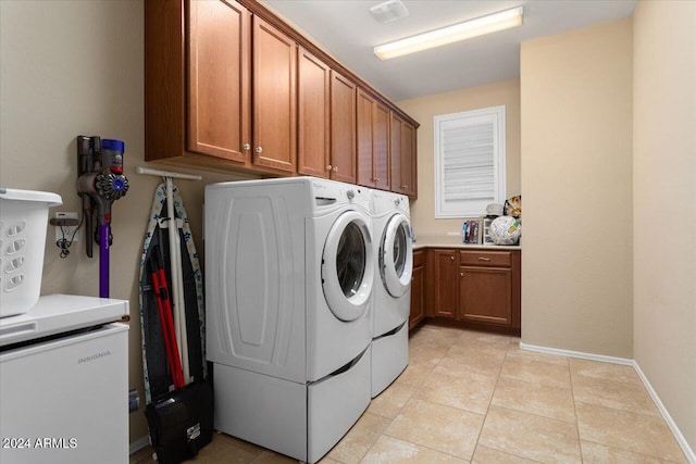 clothes washing area featuring washing machine and clothes dryer, cabinets, and light tile patterned floors