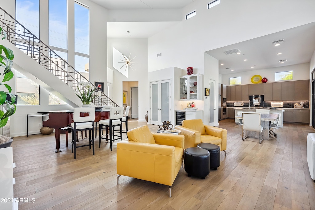 living room with a high ceiling, a wealth of natural light, light hardwood / wood-style floors, and wine cooler