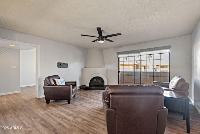 living room featuring baseboards, a tiled fireplace, a ceiling fan, wood finished floors, and a textured ceiling