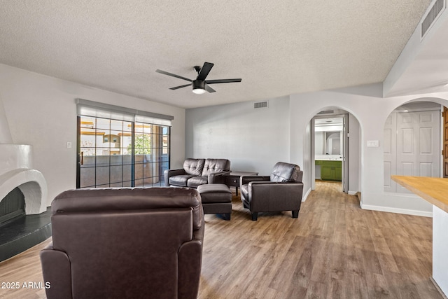 living area with arched walkways, visible vents, ceiling fan, and wood finished floors