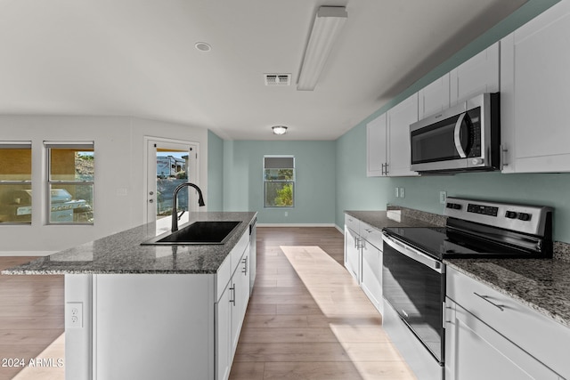 kitchen with white cabinets, stainless steel appliances, a center island with sink, and sink