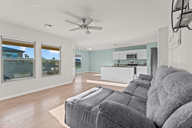 living room featuring ceiling fan, sink, and light wood-type flooring