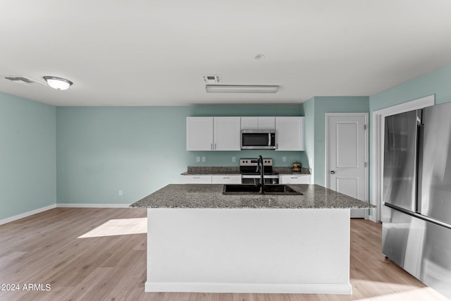 kitchen with white cabinets, appliances with stainless steel finishes, a kitchen island with sink, and dark stone countertops