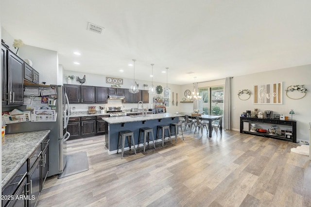 kitchen featuring appliances with stainless steel finishes, pendant lighting, an island with sink, a kitchen breakfast bar, and dark brown cabinets