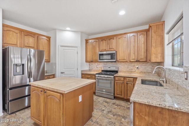 kitchen featuring appliances with stainless steel finishes, sink, backsplash, a center island, and light stone counters