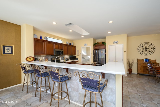 kitchen with a kitchen bar, kitchen peninsula, decorative backsplash, and stainless steel appliances