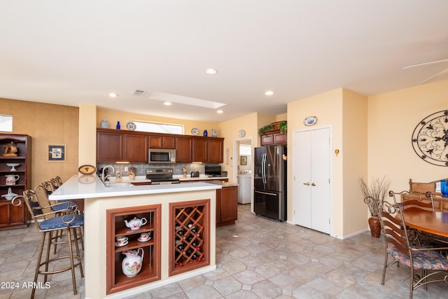 kitchen featuring kitchen peninsula, appliances with stainless steel finishes, tasteful backsplash, sink, and a breakfast bar area