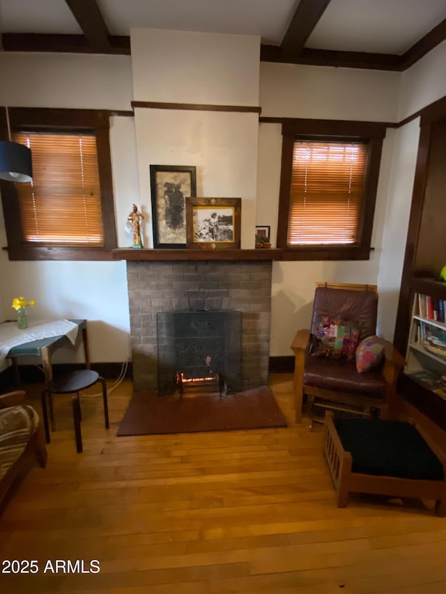 living area with a fireplace, beamed ceiling, and wood finished floors