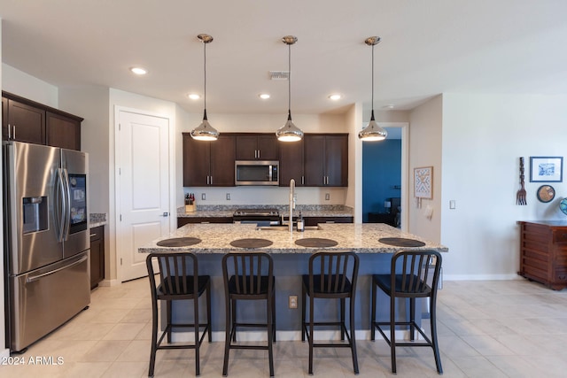 kitchen with dark brown cabinets, stainless steel appliances, a kitchen island with sink, sink, and decorative light fixtures