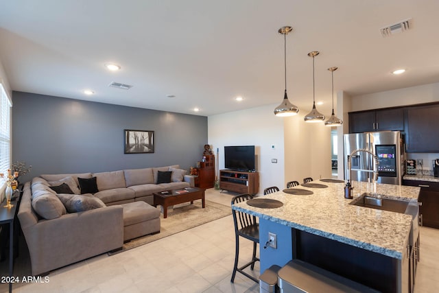 kitchen featuring light stone countertops, hanging light fixtures, stainless steel fridge with ice dispenser, a kitchen bar, and a center island with sink