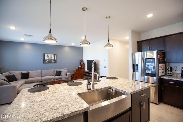 kitchen featuring light stone countertops, sink, stainless steel fridge with ice dispenser, pendant lighting, and dark brown cabinets