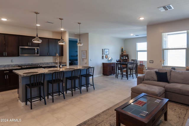 kitchen with light stone countertops, sink, pendant lighting, a kitchen bar, and a center island with sink