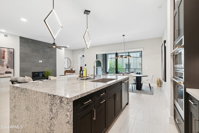 kitchen with light stone countertops, sink, decorative light fixtures, a center island with sink, and a tiled fireplace