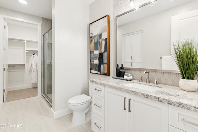 bathroom with tasteful backsplash, vanity, a shower with shower door, and toilet