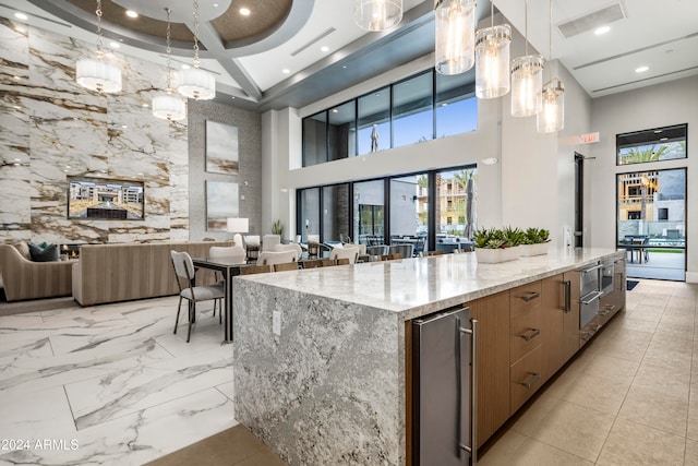 kitchen with light stone countertops, a towering ceiling, beverage cooler, decorative light fixtures, and a large island