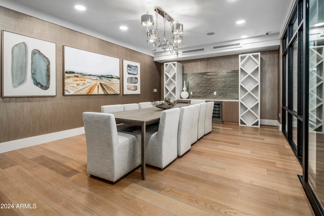 dining room with light wood-type flooring, wine cooler, and an inviting chandelier