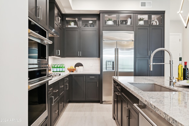 kitchen with backsplash, sink, light tile patterned floors, light stone countertops, and appliances with stainless steel finishes