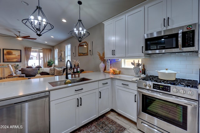 kitchen featuring pendant lighting, sink, vaulted ceiling, white cabinetry, and stainless steel appliances