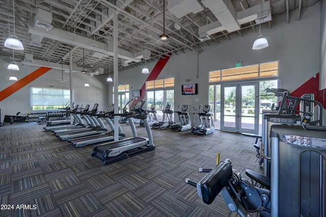 exercise room with french doors, a towering ceiling, and dark carpet