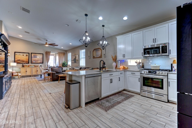 kitchen featuring appliances with stainless steel finishes, vaulted ceiling, sink, decorative light fixtures, and white cabinetry