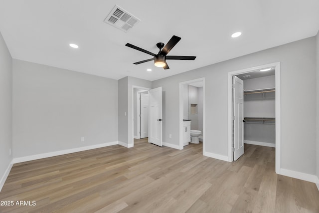 unfurnished bedroom with a spacious closet, ensuite bath, ceiling fan, and light wood-type flooring