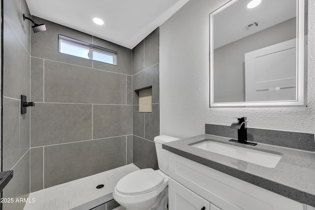 bathroom featuring vanity, toilet, and a tile shower