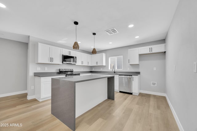 kitchen featuring white cabinetry, hanging light fixtures, light wood-type flooring, appliances with stainless steel finishes, and a kitchen island